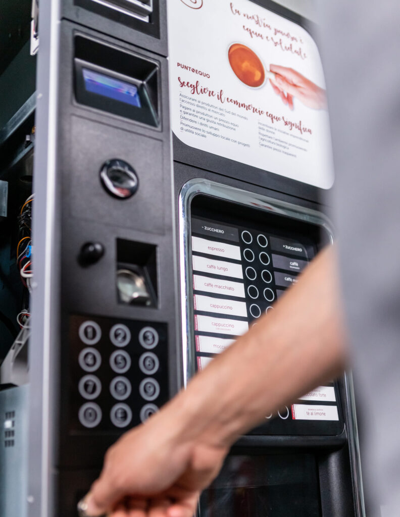 Personne utilisant un distributeur automatique de boissons chaudes, avec des options de café issu du commerce équitable de Punto Equo. Le panneau supérieur montre le message de choix du commerce équitable.