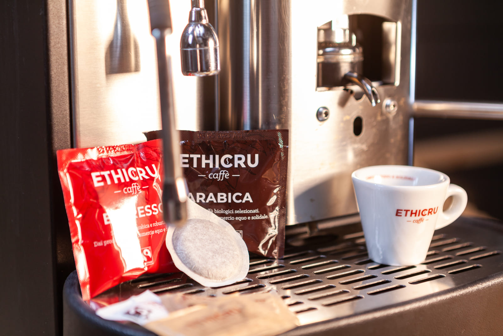 Macchina per cialde compostabili con confezioni di Ethicru Caffè Arabica e Espresso e una tazzina con logo Ethicru.
