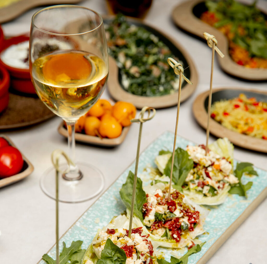 Aperitivo gourmet con bicchiere di vino bianco e snack creativi. Il piatto include foglie di insalata, pomodori secchi e formaggio, perfetto per un happy hour elegante.