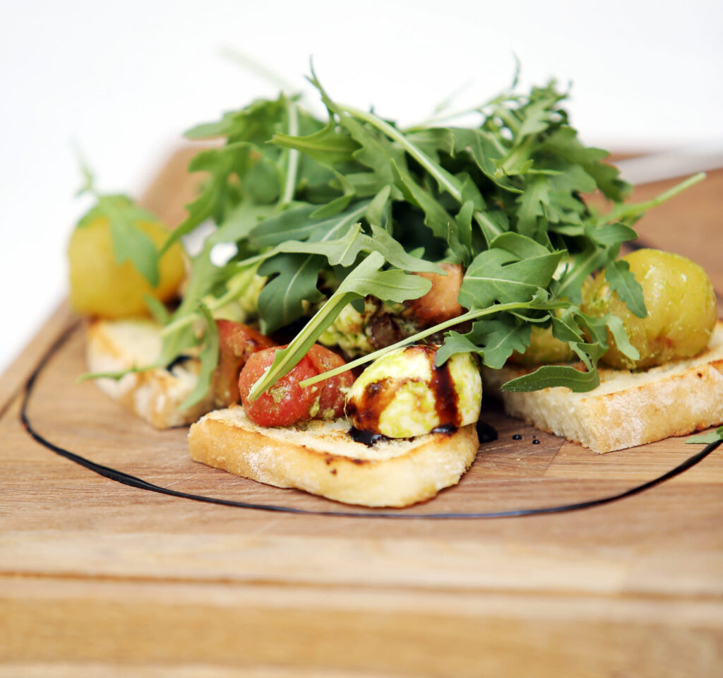 Bruschetta con rucola fresca, pomodorini e bocconcini di formaggio su pane tostato, arricchita con aceto balsamico, ideale per un antipasto italiano di qualità.