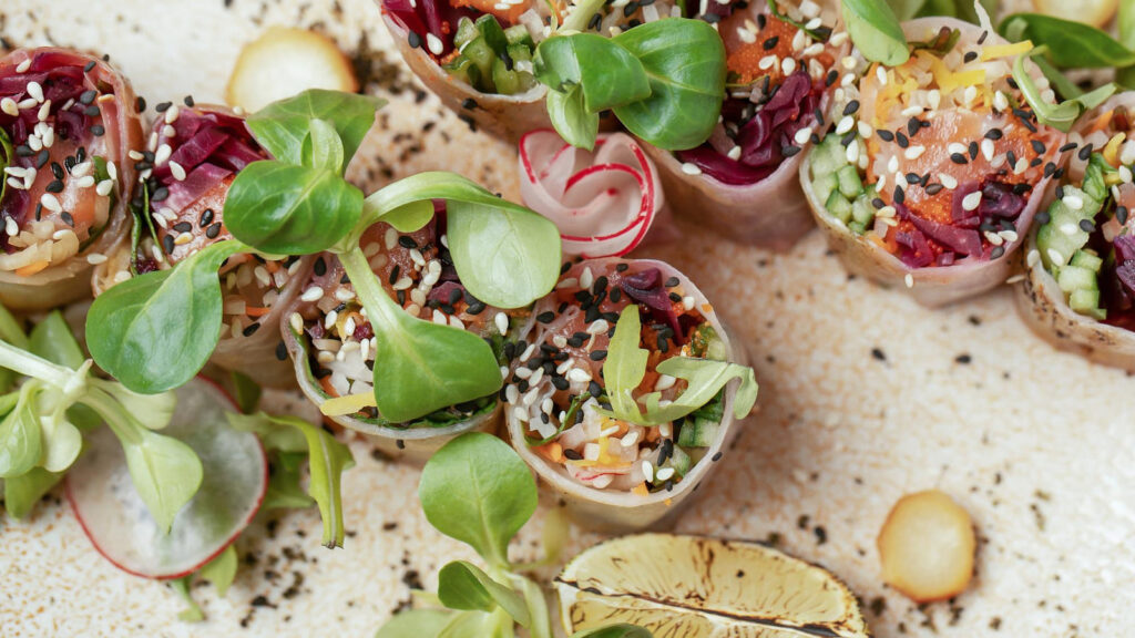 Rotolini vegetali in stile sushi vegano, guarniti con semi di sesamo e verdure fresche, su un piatto decorativo. Perfetti per una cucina sana e colorata.